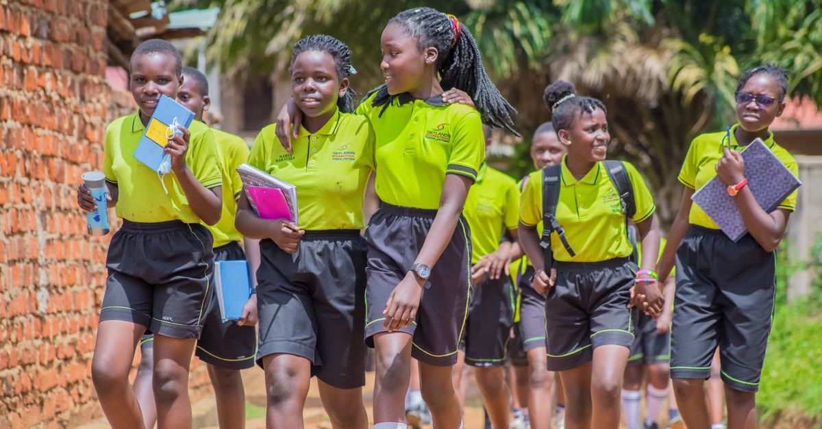 Group of smiling Ugandan students walking outdoors in school uniforms.