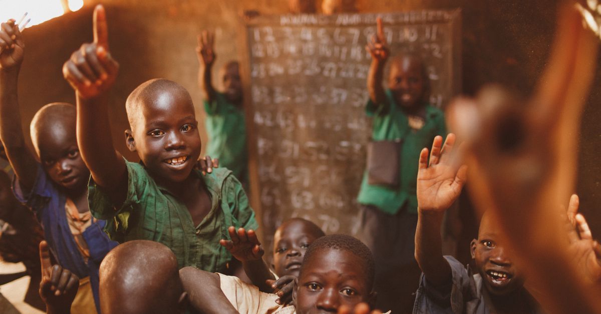 Young students in Kitgum, Uganda, enthusiastically participate in class, raising their hands with smiles.